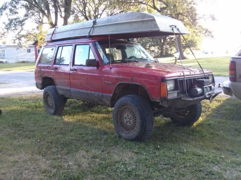 1986 Ford Bronco - This red Jeep Cherokee is equipped with a boat on its roof rack, ready for an adventure.