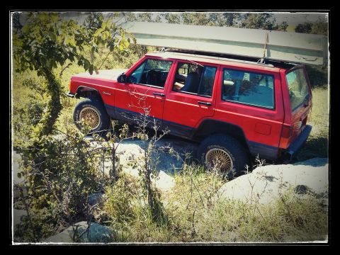 1986 Ford Bronco - This Jeep Cherokee is navigating rough terrain with a canoe secured to its roof.