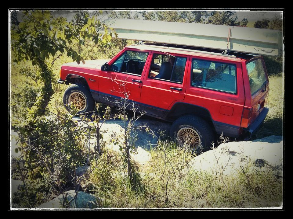 Red Jeep Cherokee XJ driving over rocks with a canoe on its roof rack