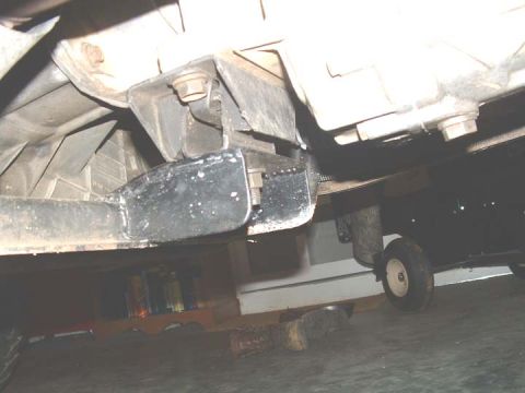1994 Ford Bronco - Underside view of a vehicle's frame and transmission mount, with a small wheel visible in the background.