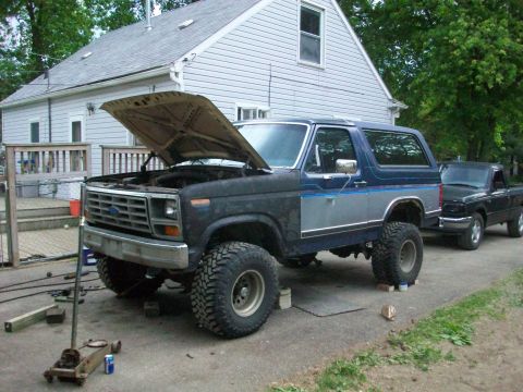 1986 Ford Bronco - 1986 Ford Bronco undergoing work, parked next to a black pickup truck in a driveway.