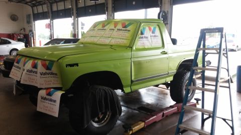 1986 Ford Bronco - A green pickup truck is being worked on in a garage, with Valvoline banners covering the windows and front.