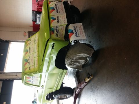1986 Ford Bronco - A green Ford Bronco is seen on a lift, covered in Valvoline promotional signs.
