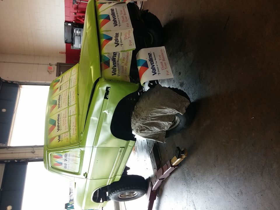 Green Ford Bronco with Valvoline signs taped to its side, lifted on a rack