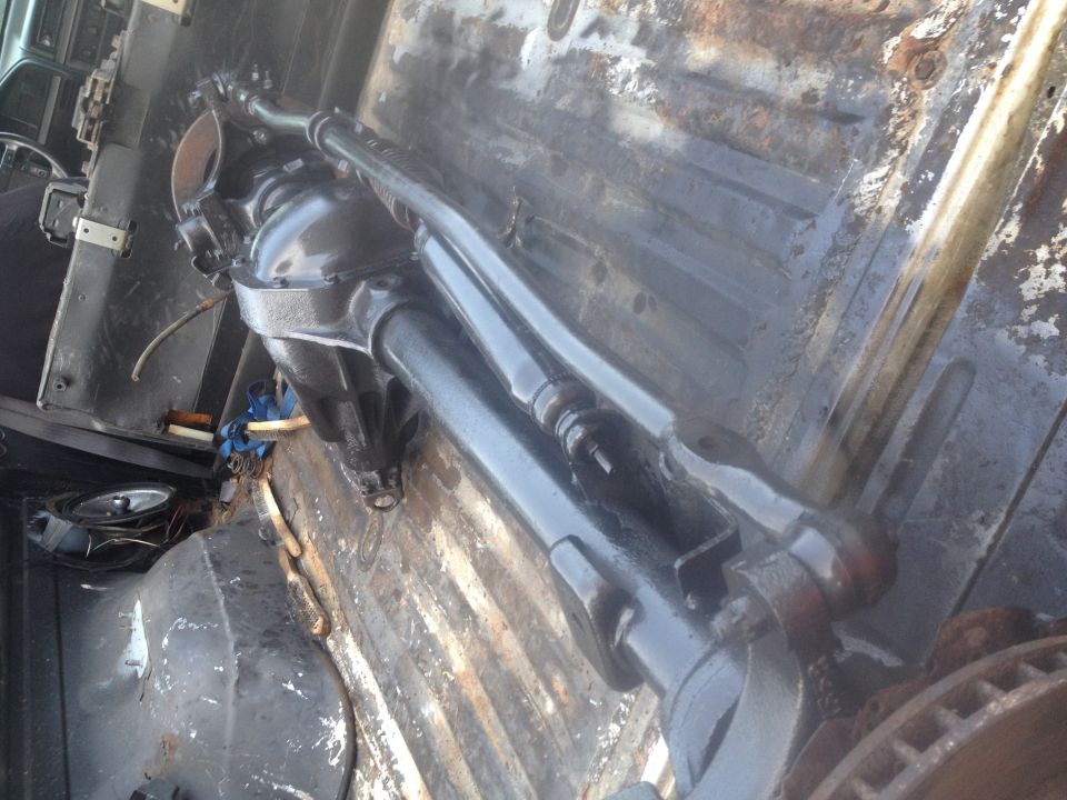 Black-painted solid front axle with differential and steering linkage in a rusty truck bed