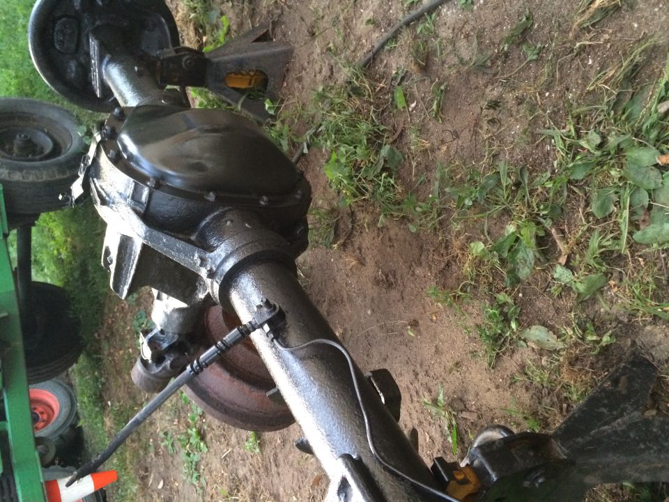 Black-painted rear axle with differential and drum brake sitting on the ground outdoors