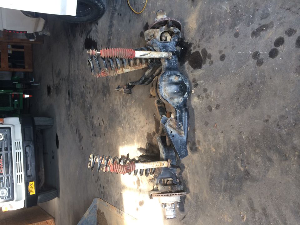 Front axle assembly with red-booted shocks and springs, resting on a concrete floor