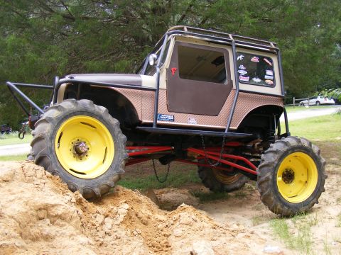 Modified off-road vehicle with large tractor tires and yellow rims, lifted suspension, and a roll cage