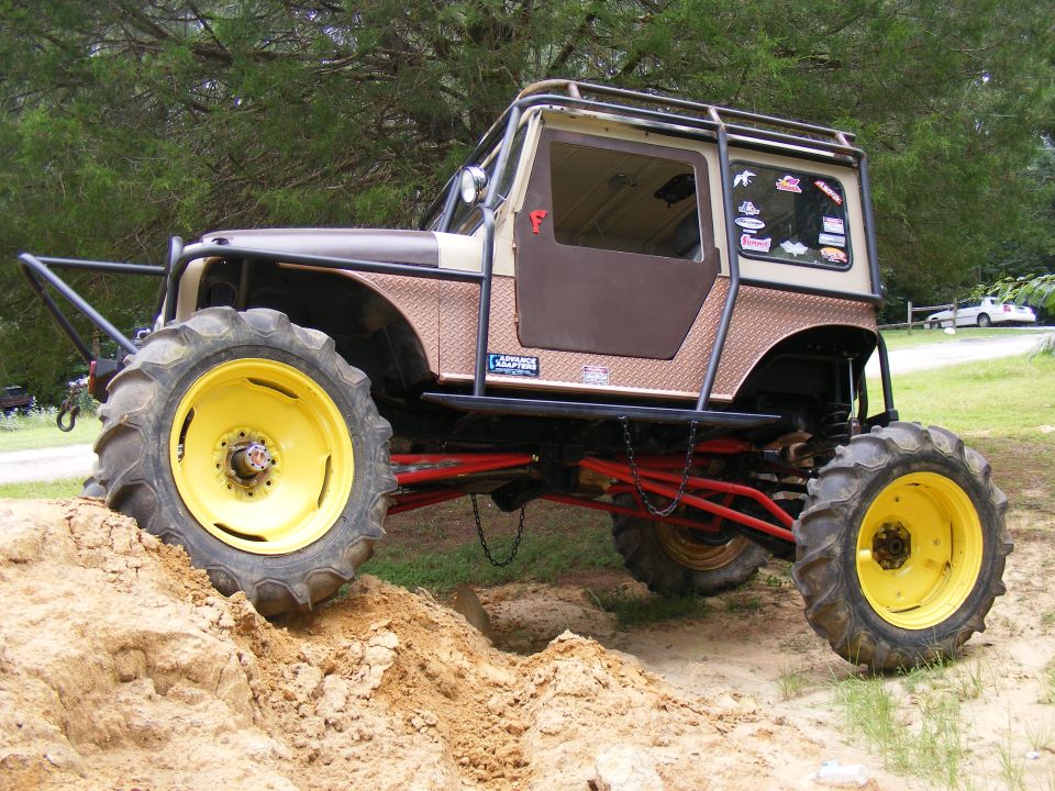 Modified off-road vehicle with large tractor tires and yellow rims, lifted suspension, and a roll cage