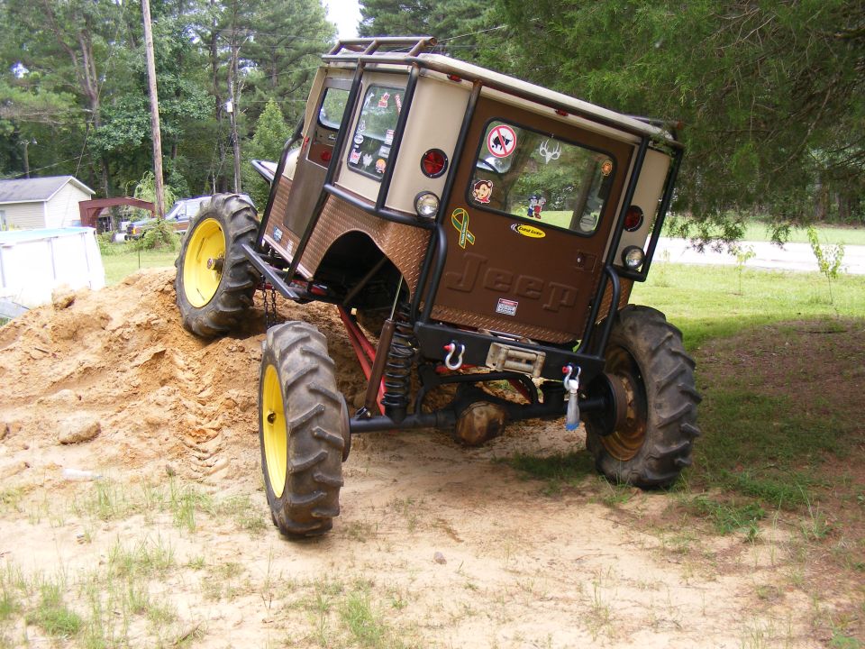 Brown Jeep CJ-series with large tractor tires climbing a dirt mound