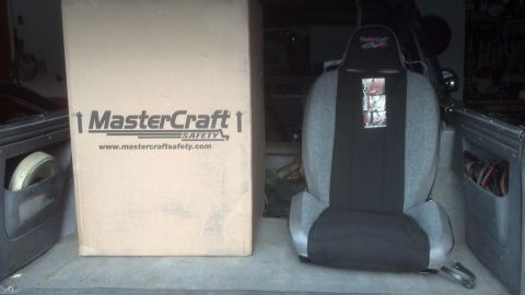 1995 Ford Bronco - A large box with MasterCraft Safety branding sits beside a racing seat, both placed within the cargo area of a vehicle.