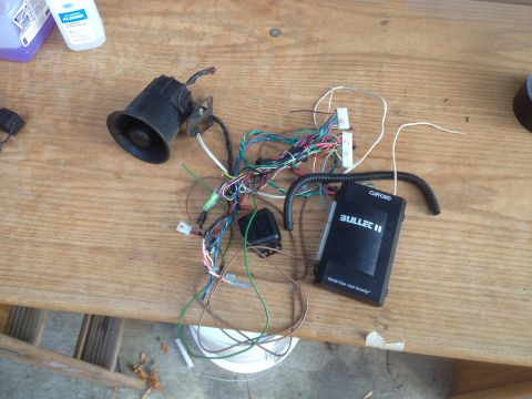 1992 Ford F-150 - Various car alarm parts are laid out on a wooden table, including a siren and a Clifford Bullet II control unit.