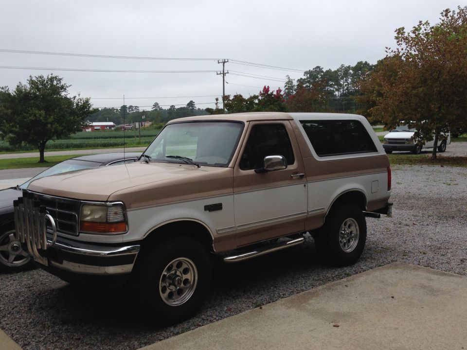 Two-tone brown and white Ford Bronco parked on gravel, front bull bar, chrome side steps