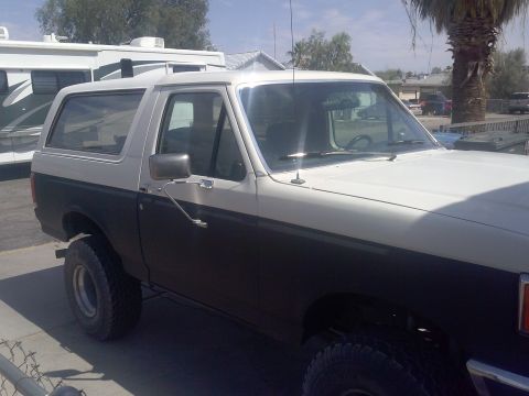 1988 Ford Bronco - This two-tone Ford Bronco is parked in a sunny outdoor lot next to an RV.