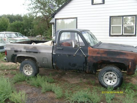 1979 GMC C/K Pickup - A weathered pickup truck sits parked next to a house, with another vehicle in the background.