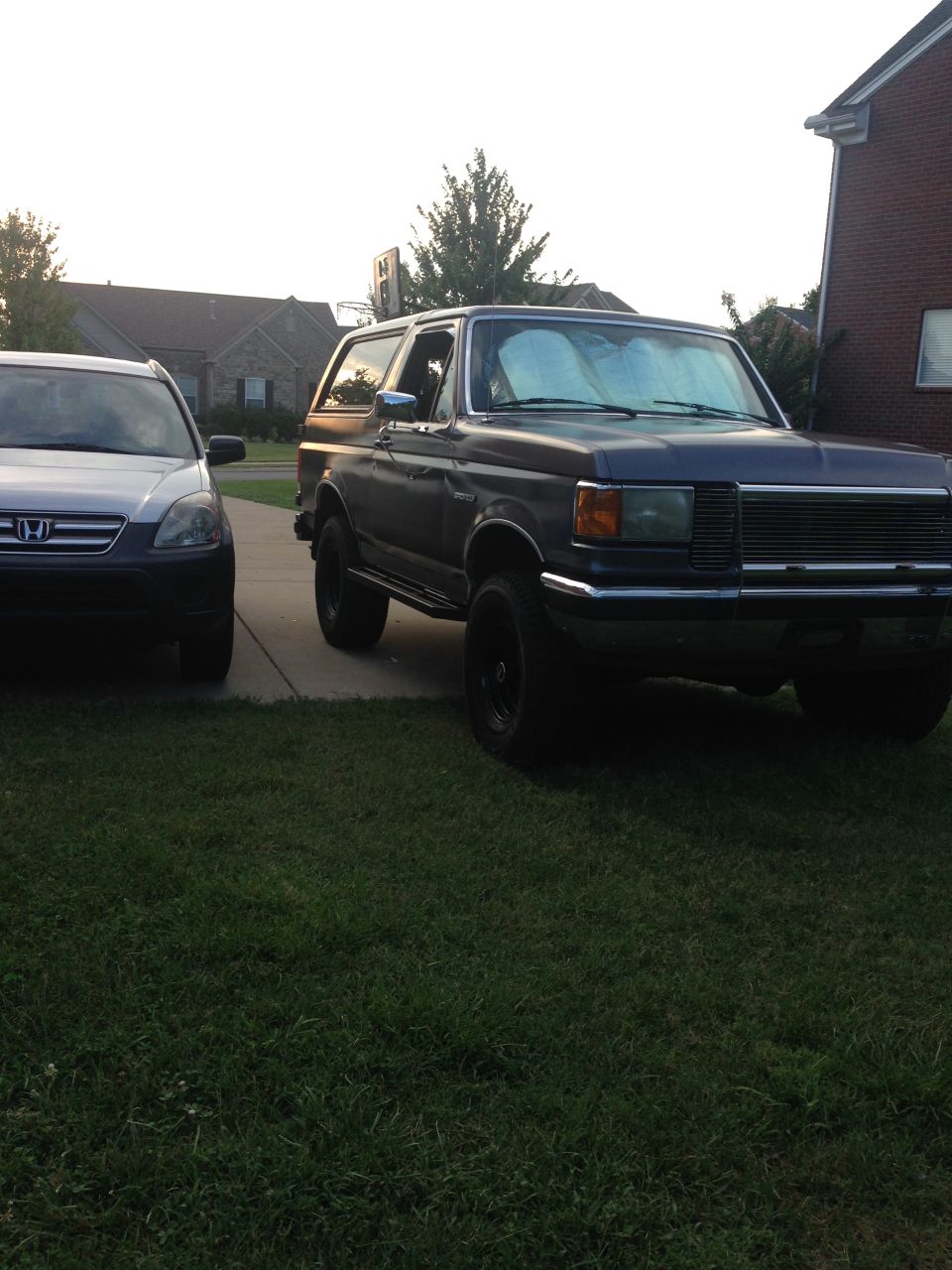 Dark blue 1990 Ford Bronco parked on driveway next to a silver SUV