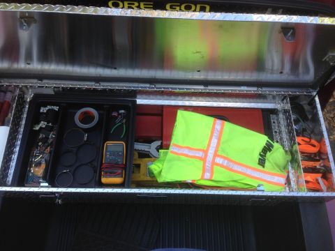 1992 Ford F-150 - A UWS toolbox in a truck bed contains various tools, including a multimeter and a safety vest, with 'ORE GON' visible on the lid.