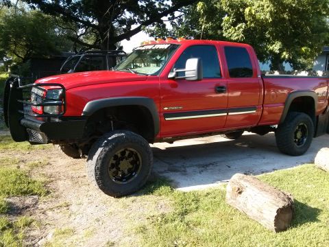 1986 Ford Bronco - A red pickup truck with a custom grille guard and lifted suspension is parked on a paved surface.