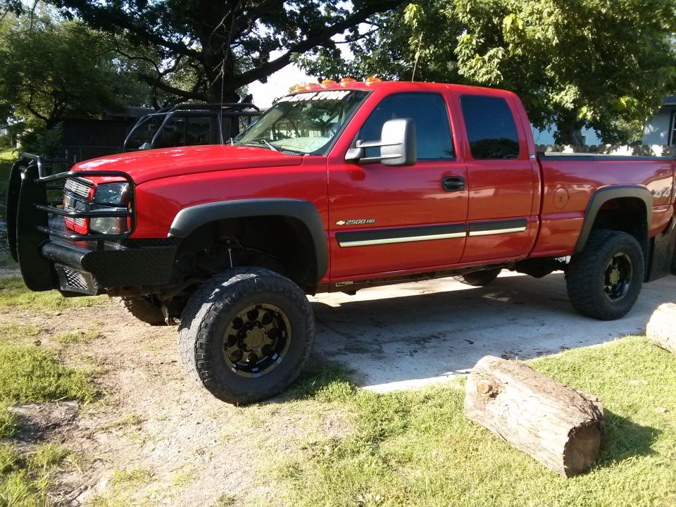 Red pickup truck with black grille guard and large tires parked outside