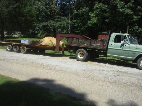 Green flatbed truck towing a trailer loaded with sand. Truck appears to be a 1973 Ford F-Series