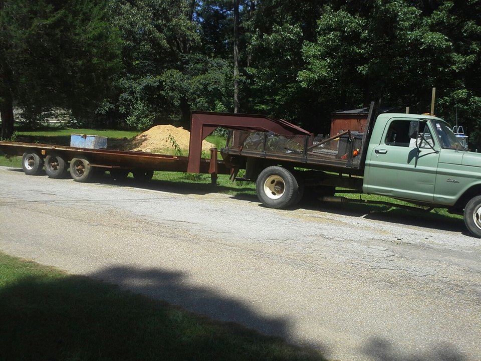 Green flatbed truck towing a trailer loaded with sand. Truck appears to be a 1973 Ford F-Series