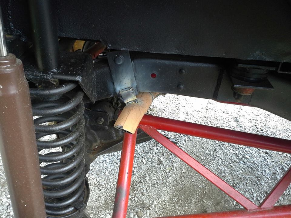 Close-up of a vehicle's suspension with a red roll cage visible. Shows a shock absorber, coil spring, and frame components