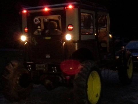 Off-road vehicle with large tires and yellow rims, rear view at night, red brake lights illuminated