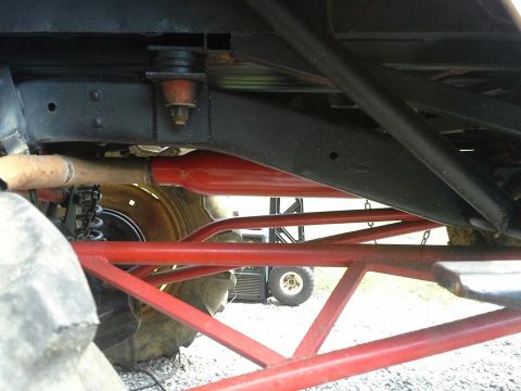 Undercarriage with red suspension components and large tire. A utility vehicle is visible in the background