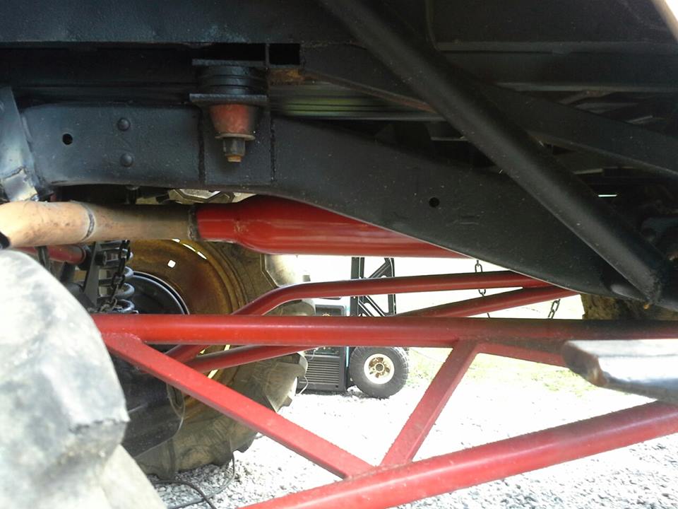 Undercarriage with red suspension components and large tire. A utility vehicle is visible in the background