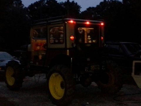 Off-road vehicle with yellow wheels and roof rack, parked next to another vehicle at dusk
