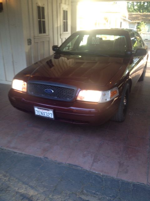 2009 Ford Crown Victoria - A red 2009 Ford Crown Victoria is parked under a carport, showing its front end and license plate.