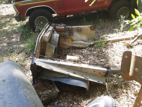 1978 Ford Bronco - Disassembled vehicle parts are scattered on the ground near a red truck.