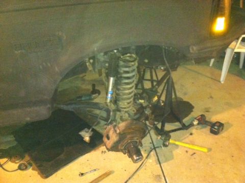1995 Ford Bronco - The front suspension of a vehicle is shown disassembled, with tools and parts scattered around.