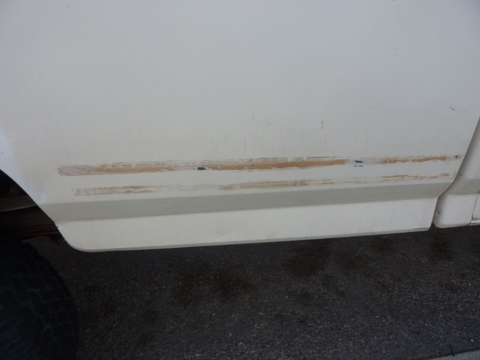 White truck lower body panel showing rust and paint damage along a trim line