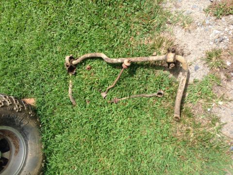 1979 Ford Bronco - Various suspension components, including a sway bar, lie on the grass next to a tire.