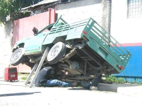 1996 Ford Bronco - A person is welding the frame of a green pickup truck that is elevated on metal stands.