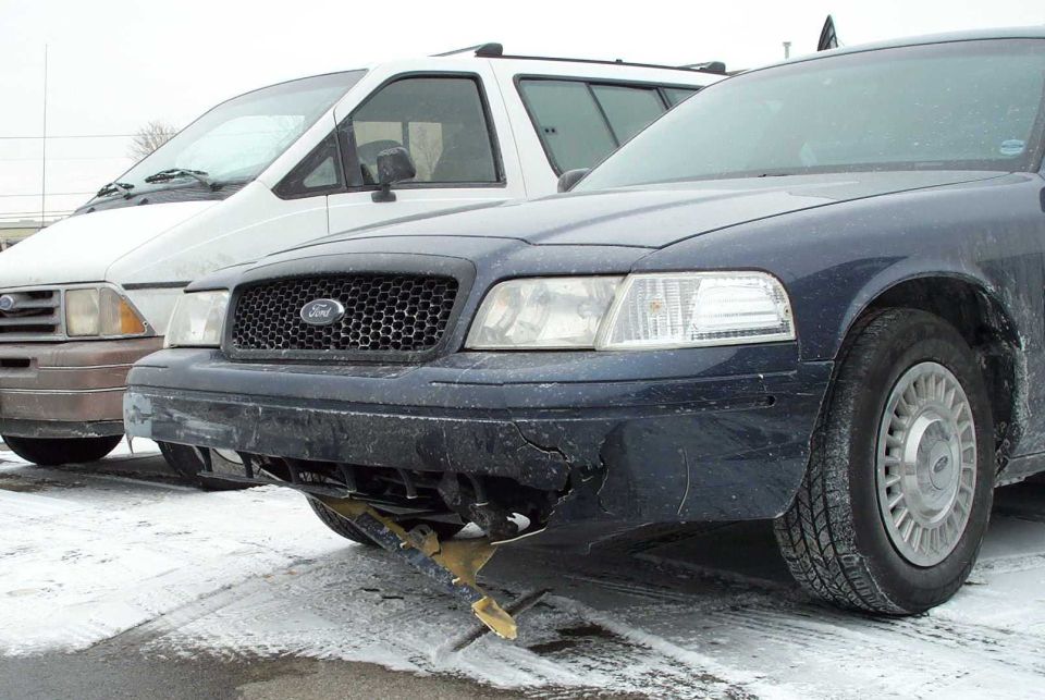 Dark blue Ford Crown Victoria front with damaged bumper in snowy lot