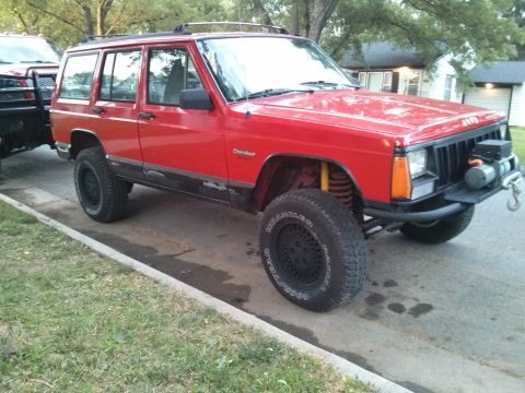 1986 Ford Bronco - A red Jeep Cherokee XJ is parked on a street, partially obscuring a trailer.