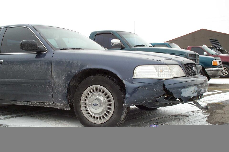 Dark blue sedan with damaged front bumper, parked in a lot with other vehicles