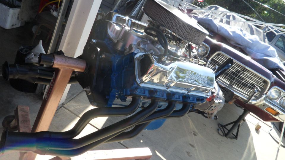V8 engine on stand, headers attached. Car body visible behind
