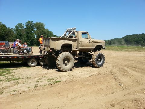 1996 Ford Bronco - A lifted truck with oversized tires is parked on a trailer at an outdoor event.
