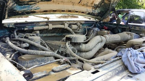 1996 Ford Bronco - The engine bay of a vehicle is heavily covered in mud, with another vehicle partially visible in the background.