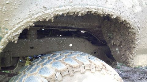 1996 Ford Bronco - This close-up shot shows the heavily mud-caked undercarriage and tire of a vehicle.