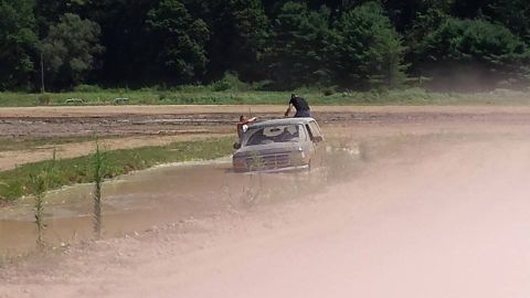 1996 Ford Bronco - A gray Ford Bronco is stuck in a muddy area with two people on its roof.