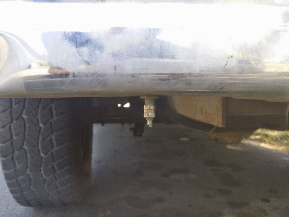 Close-up of a tire valve stem hanging below a chrome bumper