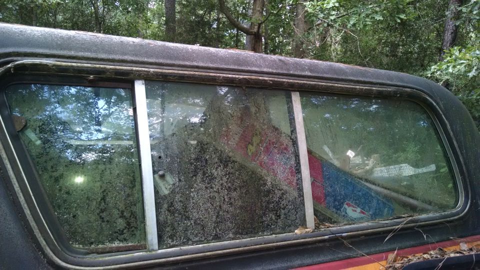 Rear window of a 1978 Ford Bronco with reflections and debris