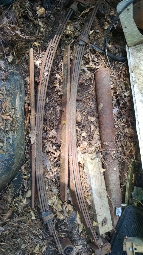 1978 Ford Bronco - Discarded vehicle parts, including leaf springs and a tire, lie on the ground amidst debris.