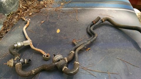 1978 Ford Bronco - Various engine hoses and metal pipes are shown resting on a dark surface, possibly a vehicle's hood, covered in pine needles.