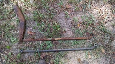 1978 Ford Bronco - Two metal linkage rods and a rusted exhaust pipe section are shown on the ground.