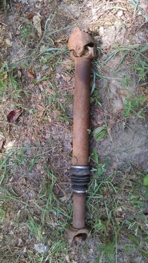 1978 Ford Bronco - A single, heavily rusted driveshaft lies on the ground amidst grass and dirt.